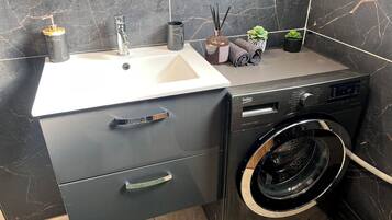 Une petite salle de bain comprenant un lavabo, un lave-linge et un meuble avec des tiroirs.