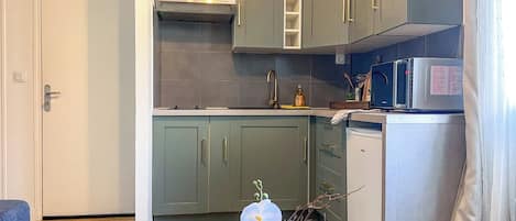 Una cocina compacta con armarios grises, un lavamanos de acero inoxidable y un refrigerador pequeño.