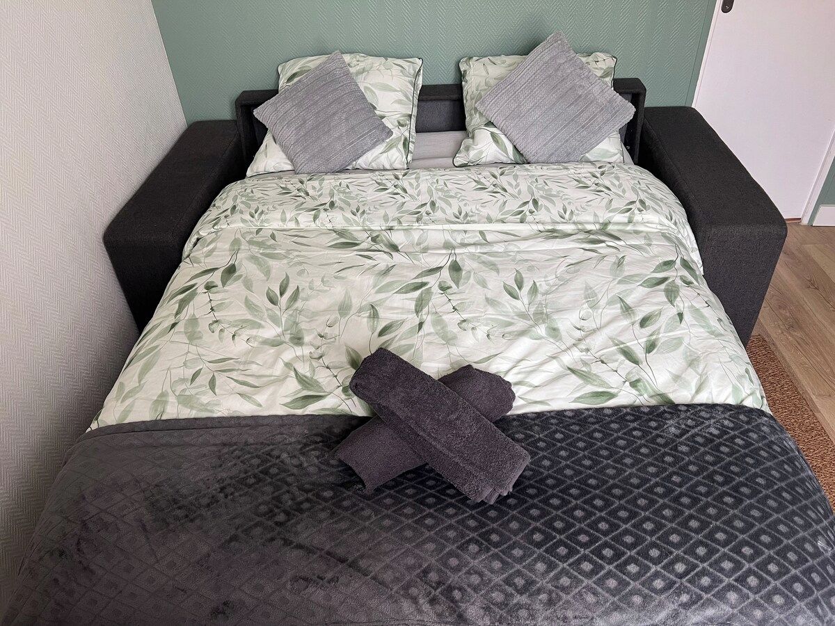 Una cama con colcha estampada de hojas, dos almohadas y una manta oscura.