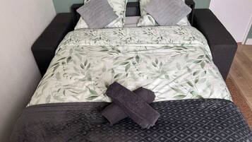 Una cama con colcha estampada de hojas, dos almohadas y una manta oscura.