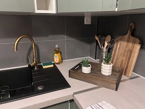 A kitchen with a black sink, a gold faucet, a bottle of dish soap, a wooden cutting board, and a tray with a potted plant.
