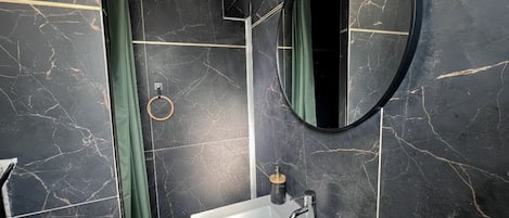 A modern bathroom with a marble sink, a round mirror, and a towel rack.