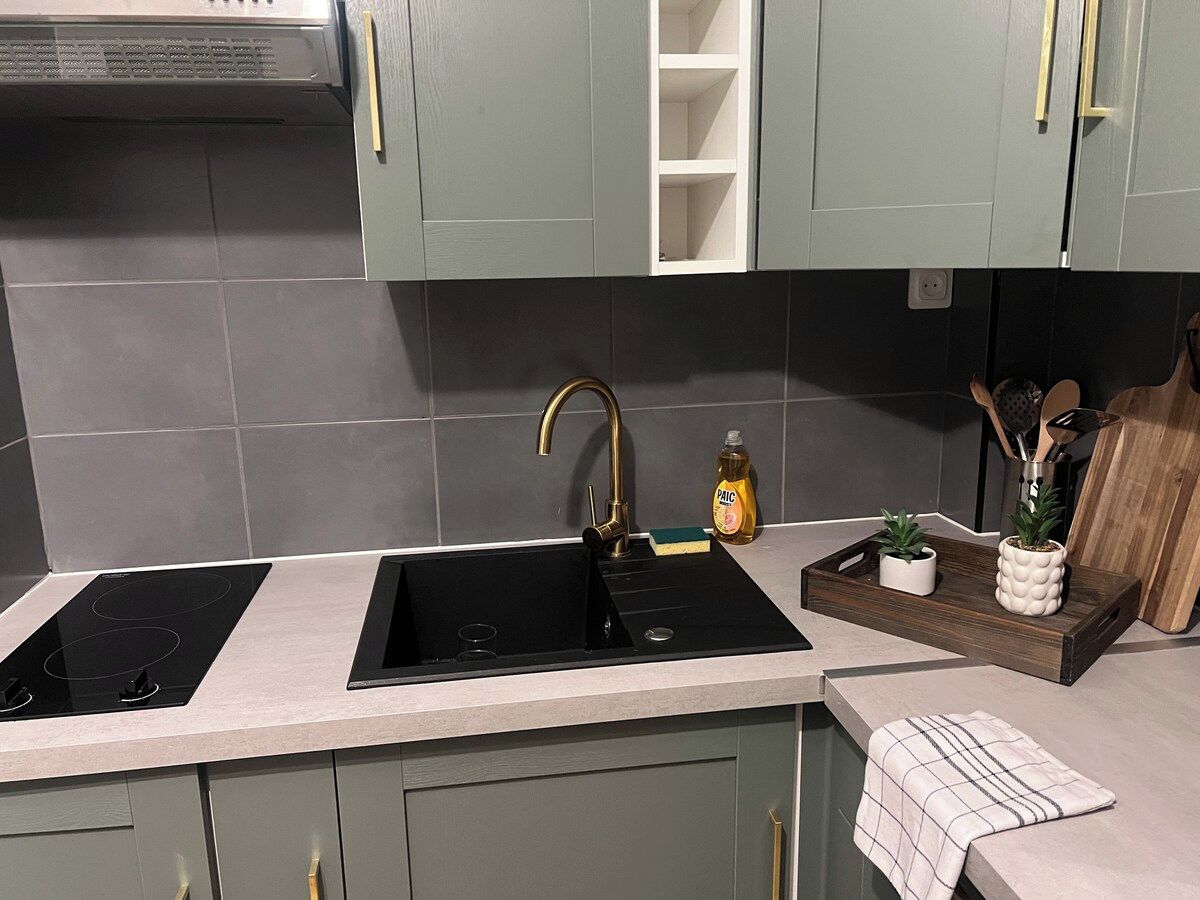 Une cuisine dotée de deux plaques de cuisson à induction noires, d’un robinet doré et d’un plateau en bois sur lequel sont disposées des plantes.