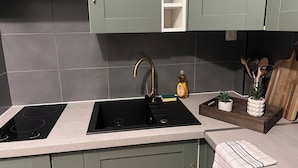 Una cocina con dos hornillas de inducción negras, un grifo dorado y una bandeja de madera con plantas.