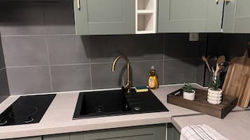 Une cuisine dotée de deux plaques de cuisson à induction noires, d’un robinet doré et d’un plateau en bois sur lequel sont disposées des plantes.