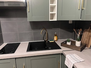 Una cocina con dos hornillas de inducción negras, un grifo dorado y una bandeja de madera con plantas.