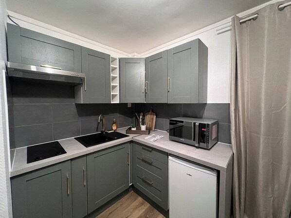 Una cocina compacta con gabinetes grises, una campana extractora de acero inoxidable, un microondas y un refrigerador pequeño.