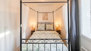 Una cama con dosel, un edredón estampado con motivos florales, dos lámparas de noche y un candelabro en el techo.