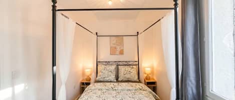 Una cama con dosel, un edredón estampado con motivos florales, dos lámparas de noche y un candelabro en el techo.