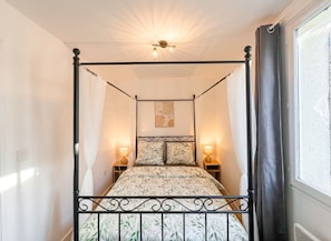 Una cama con dosel, un edredón estampado con motivos florales, dos lámparas de noche y un candelabro en el techo.