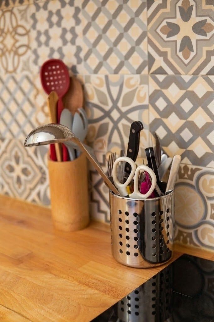 Ein Küchenutensilienhalter mit verschiedenen Utensilien auf einer Holzauskleidung vor einer gemusterten Spritzschutzwand.
