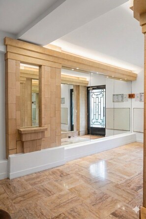 Un'ampia stanza con un grande specchio, una porta decorata con un motivo geometrico e un pavimento piastrellato.
