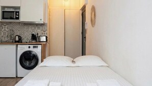 Ein Hotelzimmer mit einem Bett, zwei Kissen, einer Waschmaschine, einer Mikrowelle und einer Kaffeemaschine.