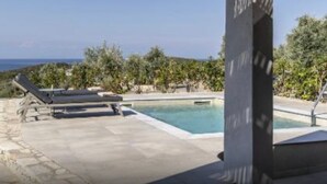 Zona de piscina con sillones de descanso y vista al mar.