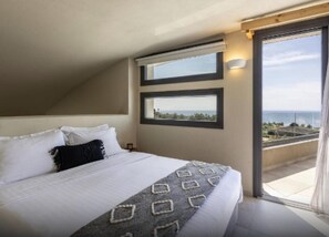A bedroom with a large bed, two windows, and a view of the sea.