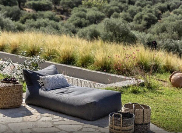 Un espace extérieur aménagé avec un canapé de couleur sombre, deux coussins et un panier en osier.