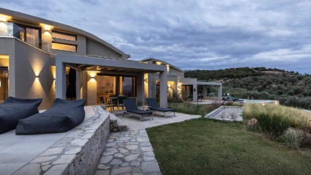 Una casa moderna con un patio de piedra, mobiliario exterior y vistas a un paisaje montañoso.