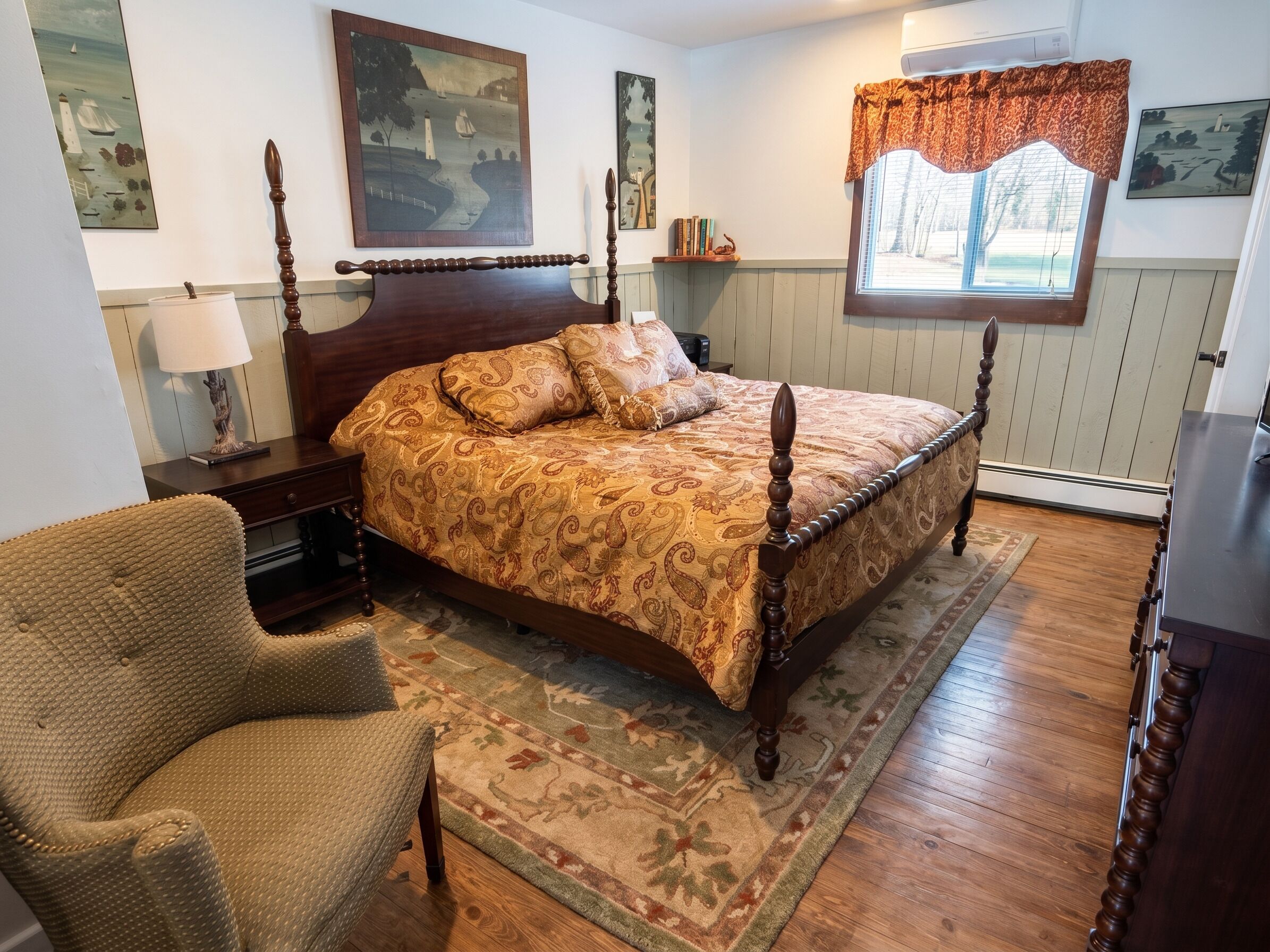 A bedroom with a wooden four-poster bed, a chair, a rug, and artwork on the walls.
