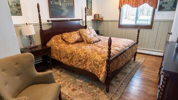 A bedroom with a wooden four-poster bed, a chair, a rug, and artwork on the walls.