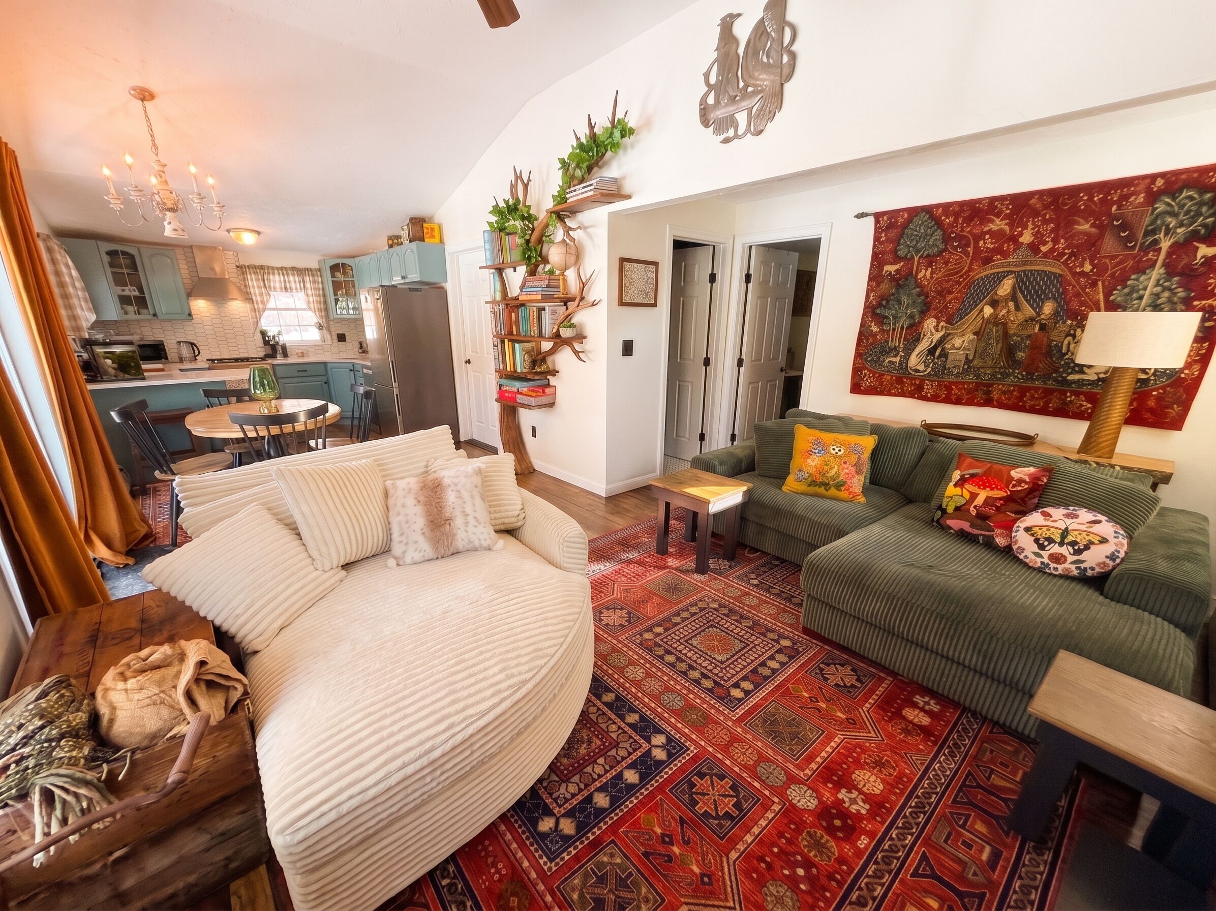 A cozy living room with a round beige sofa, a green sofa with patterned cushions, and a red patterned rug.