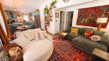 A cozy living room with a round beige sofa, a green sofa with patterned cushions, and a red patterned rug.