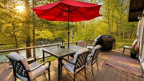 En terrasse med et bord, stole, en rød parasol og en grill.