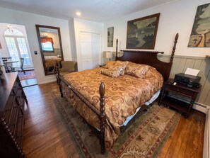 A bedroom with a large bed, a wooden dresser, a desk, and a chair. There is a door leading to another room and a window with curtains. - Tree-Lined Cottage • Wood Fireplace • Ellis River • Private Firepit • Riverside (Bartlett)