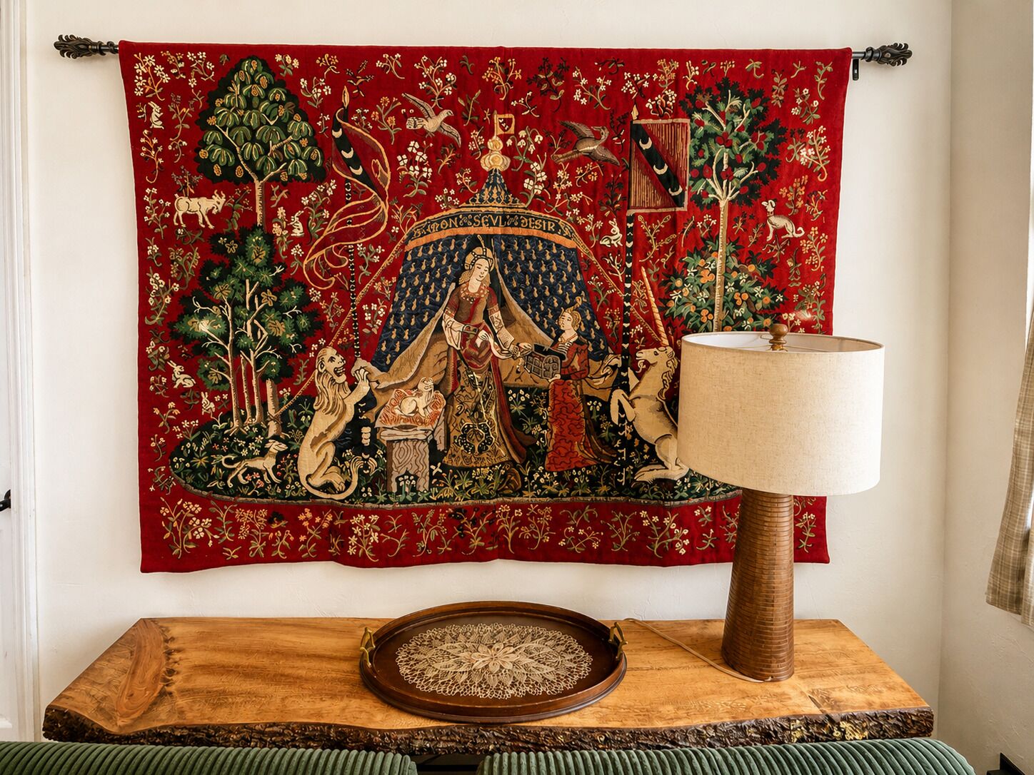 A tapestry with a central figure, a wooden table with a tray, and a lamp.