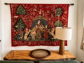 A tapestry with a central figure, a wooden table with a tray, and a lamp. - Tree-Lined Cottage • Wood Fireplace • Ellis River • Private Firepit • Riverside (Bartlett)