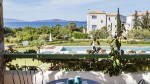 Eine Terrasse mit Tisch und Stühlen mit Blick auf einen Pool und ein Gebäude, das Meer überblickt.