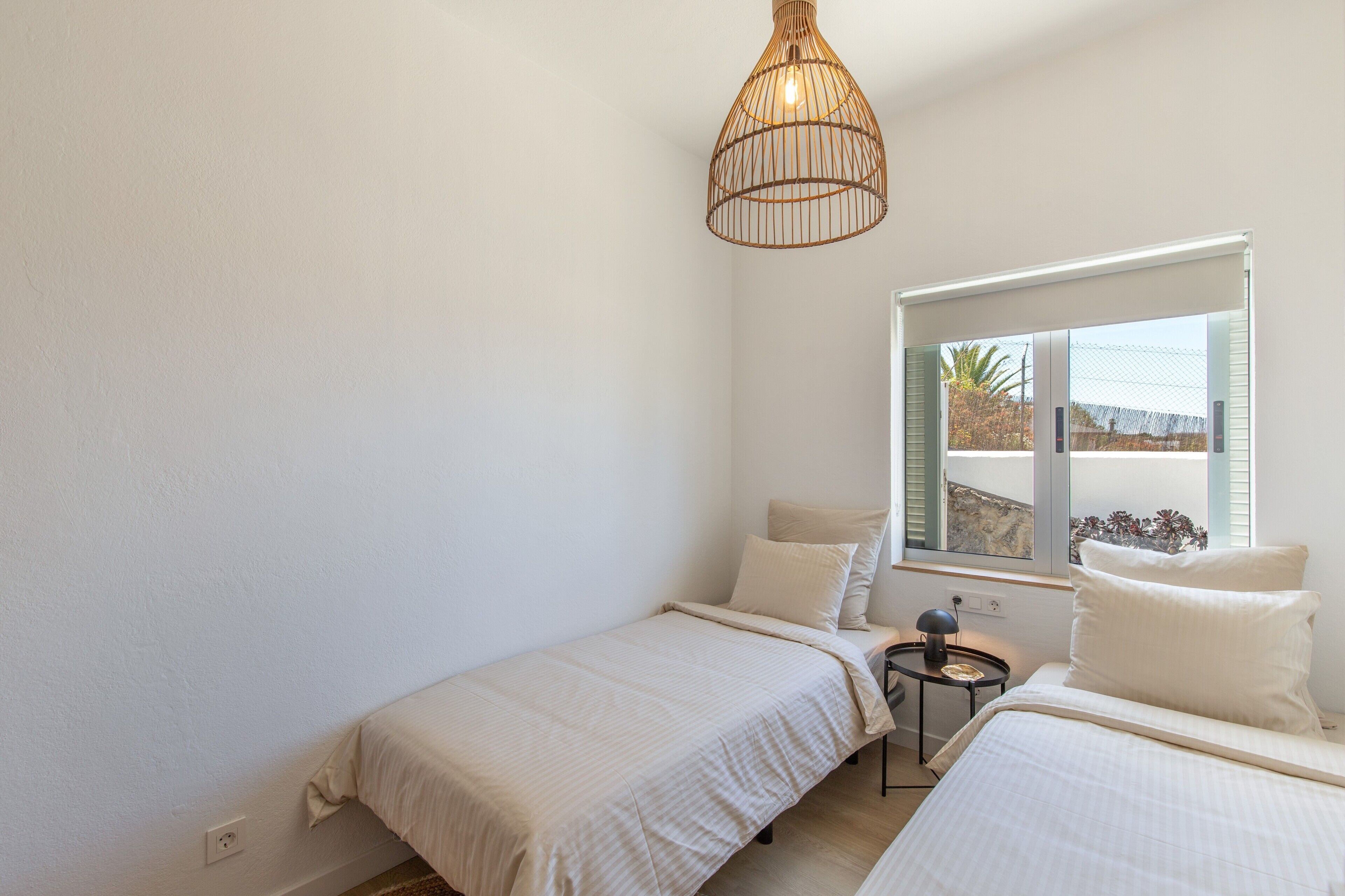 Ein Schlafzimmer mit zwei Betten, einem Fenster mit Jalousien, einer Pendelleuchte und einem kleinen Nachttisch.