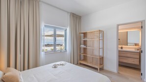 Une chambre à coucher avec un lit, une armoire en bois, une salle de bain avec un miroir et une vue sur l’extérieur.