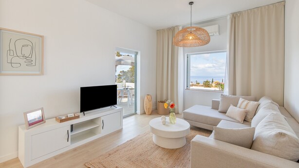 Una sala moderna con una televisión de pantalla plana, un sofá, una mesa de centro y un ventanal con vistas.