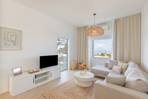 A modern living room with a flat-screen TV, a sofa, a coffee table, and a large window with a view.