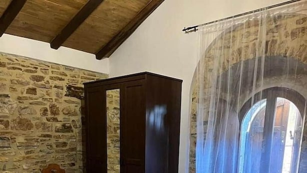 Un dormitorio con pared de piedra, una cama con ropa blanca y un ventanal con vistas.