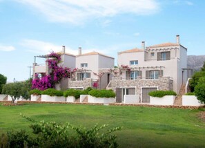 Una casa de dos pisos con fachada de piedra, múltiples ventanas y un jardín bien cuidado con flores de buganvilla.