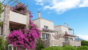 Un bâtiment à deux étages, doté de piliers en pierre et d’une pergola ornée de fleurs roses.