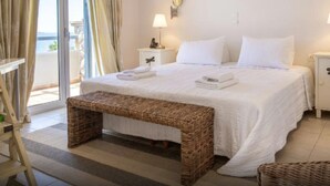 Une chambre d’hôtel avec un lit, une banquette, une table de chevet, une lampe et une vue sur la mer par la fenêtre.