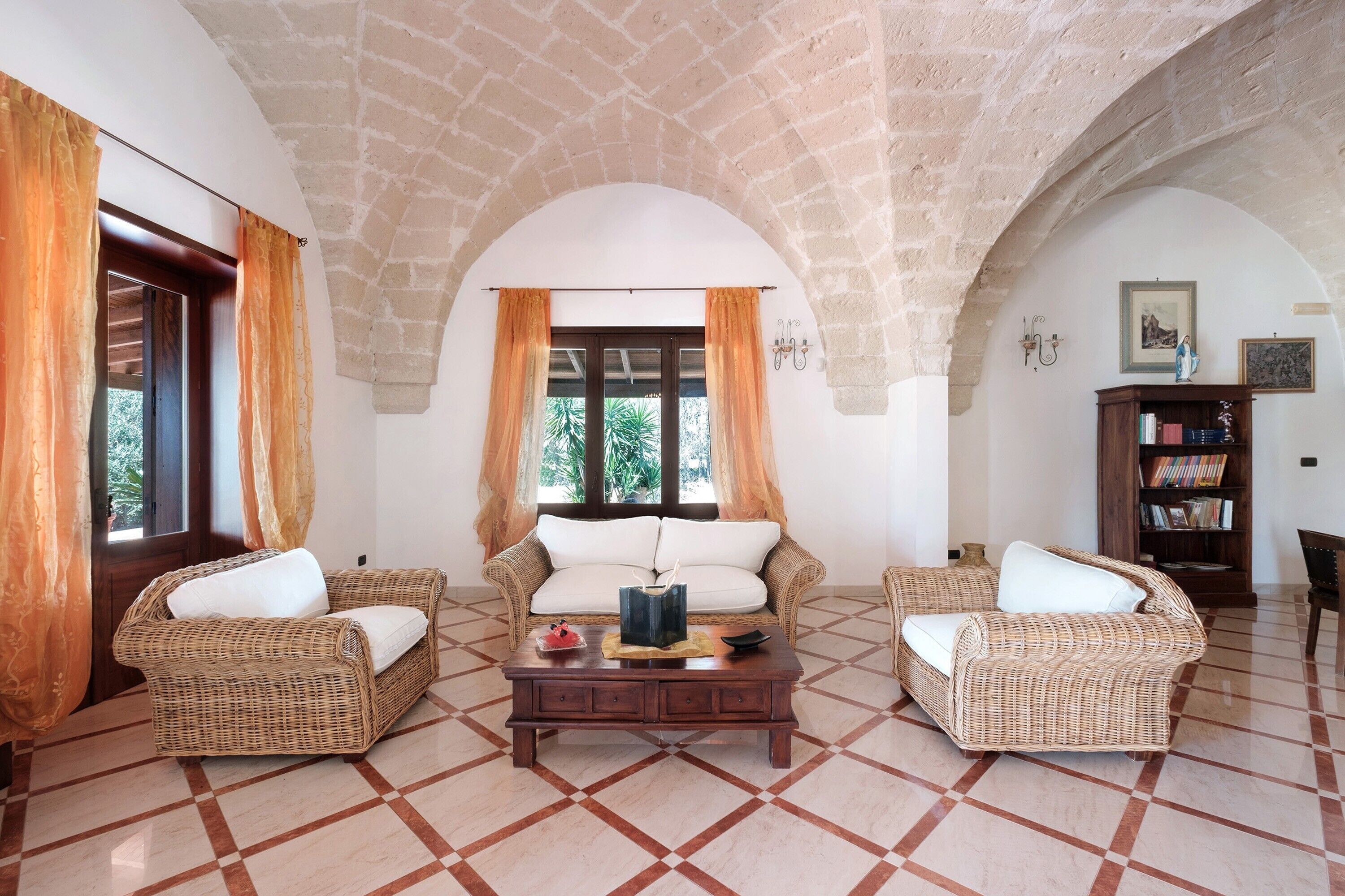 A room with a stone ceiling, a white sofa, two wicker armchairs, a wooden coffee table, and a bookshelf.