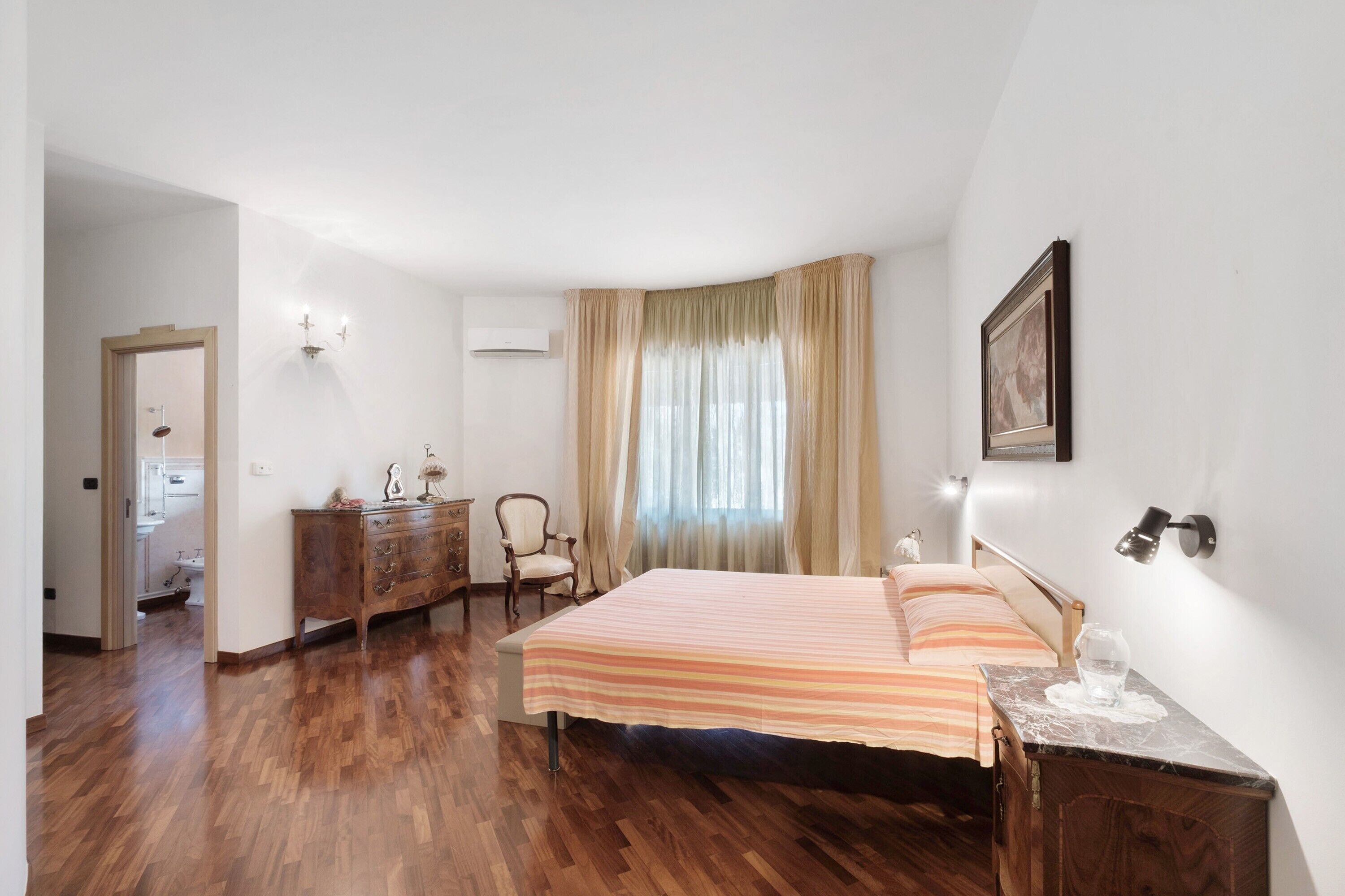 A bedroom with a bed, wooden dresser, chair, and a nightstand with a lamp.