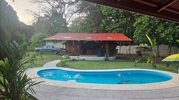 A swimming pool with a red-roofed structure in the background. - Dragon Majick (Pavones)