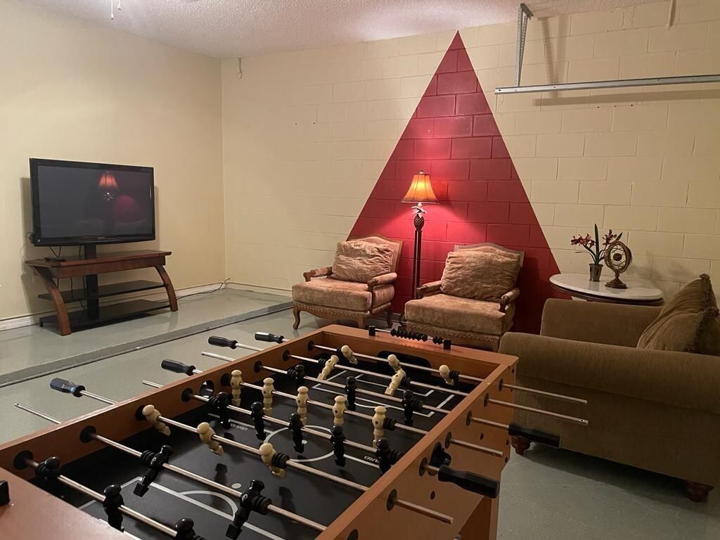 Ett vardagsrum med ett fotbollsspel, en tv, två fåtöljer, en soffa och en röd, triangulär väggdekoration.