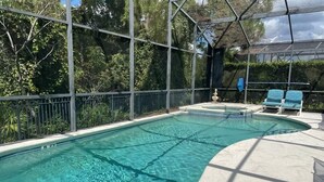 Una piscina con borde curvo, rodeada por una cerca metálica y una zona cubierta con sillas azules.