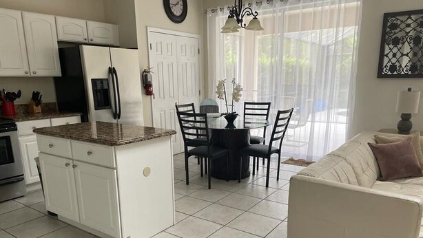 Una cocina con armarios blancos, un refrigerador y un comedor con mesa y sillas.