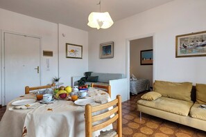 A dining area with a table set for breakfast, a sofa, and a painting on the wall. - Talamone Apartment View by Mamo Florence (Talamone)