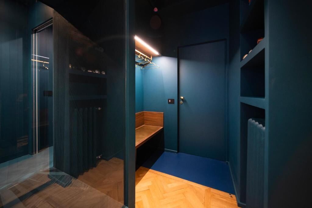 Ein Zimmer mit blauer Wand, einer hölzernen Bank, einem Heizkörper und einer Tür mit Griff.