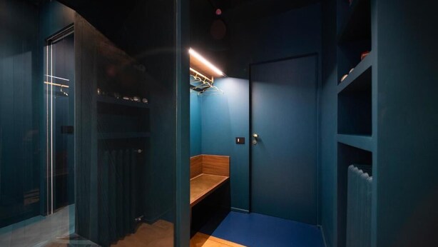 A room with a blue wall, a wooden bench, a radiator, and a door with a handle. - Fontana 16 Rooms (Milan)