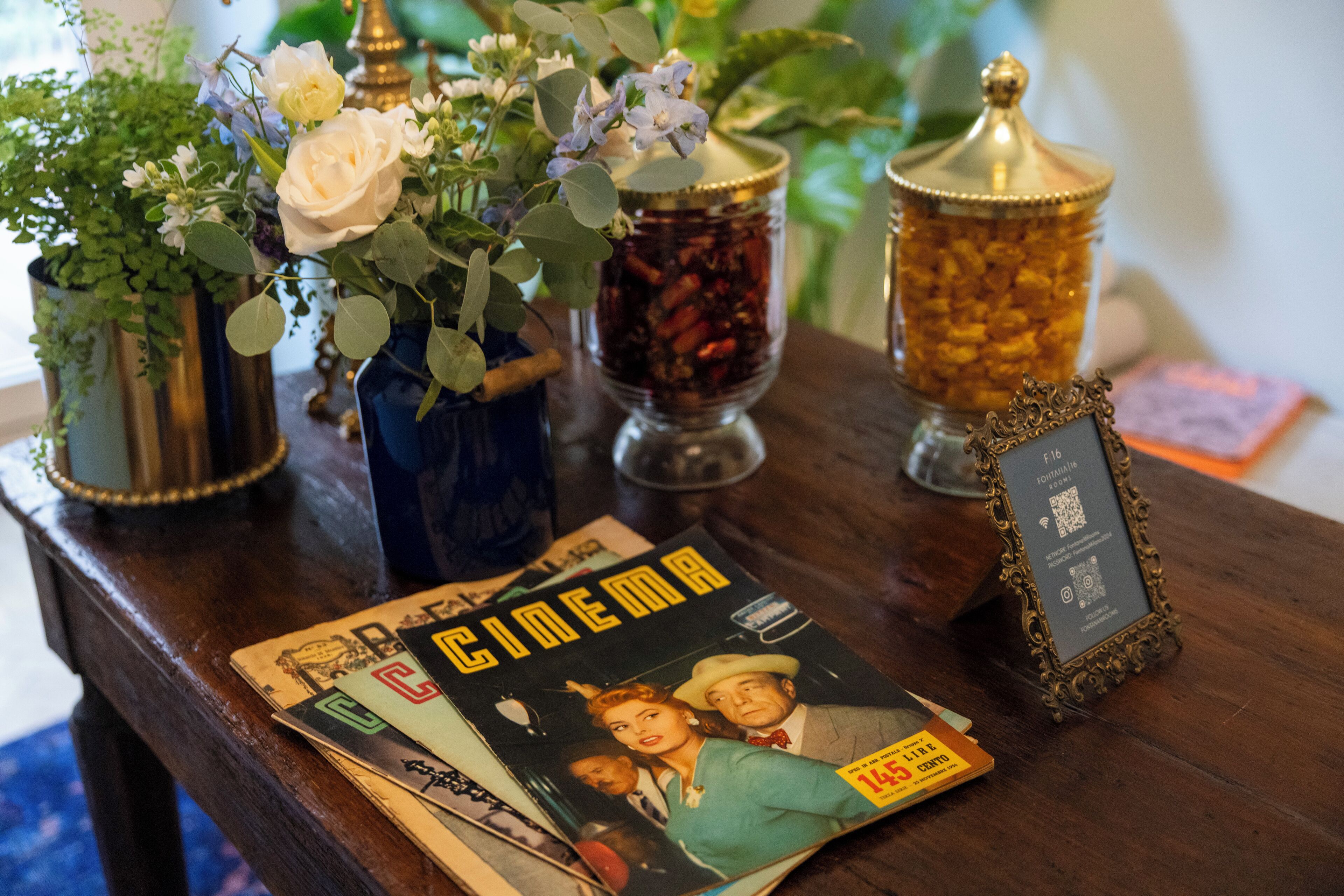 Una mesa con un cartel de cine antiguo, un código QR enmarcado y jarrones decorativos con flores y hierbas secas.