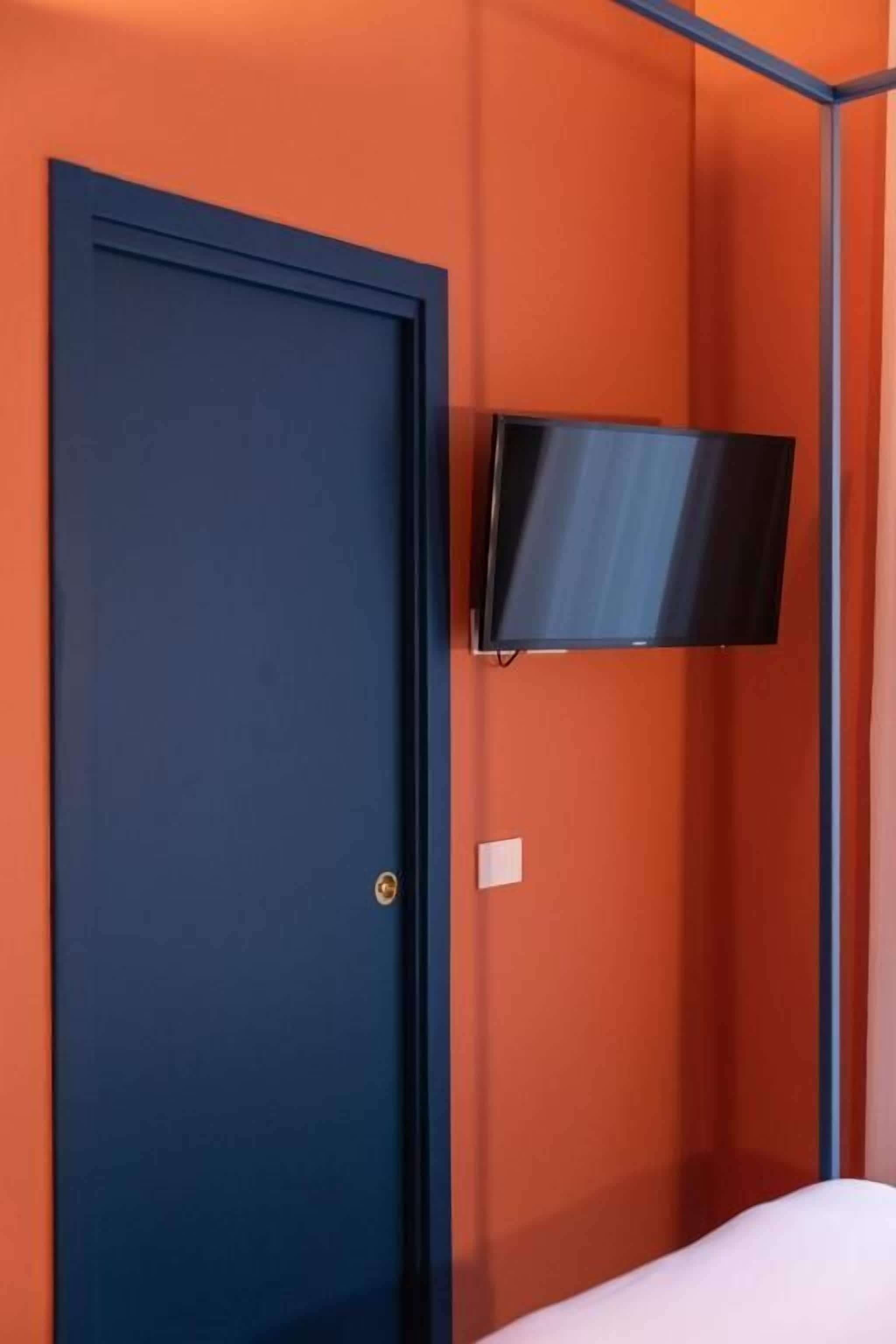 A room with a dark blue door, an orange wall, and a mounted flat-screen TV.