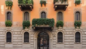 A building with arched windows, a central entrance with a decorative arch, and balconies with greenery. - Fontana 16 Rooms (Milan)